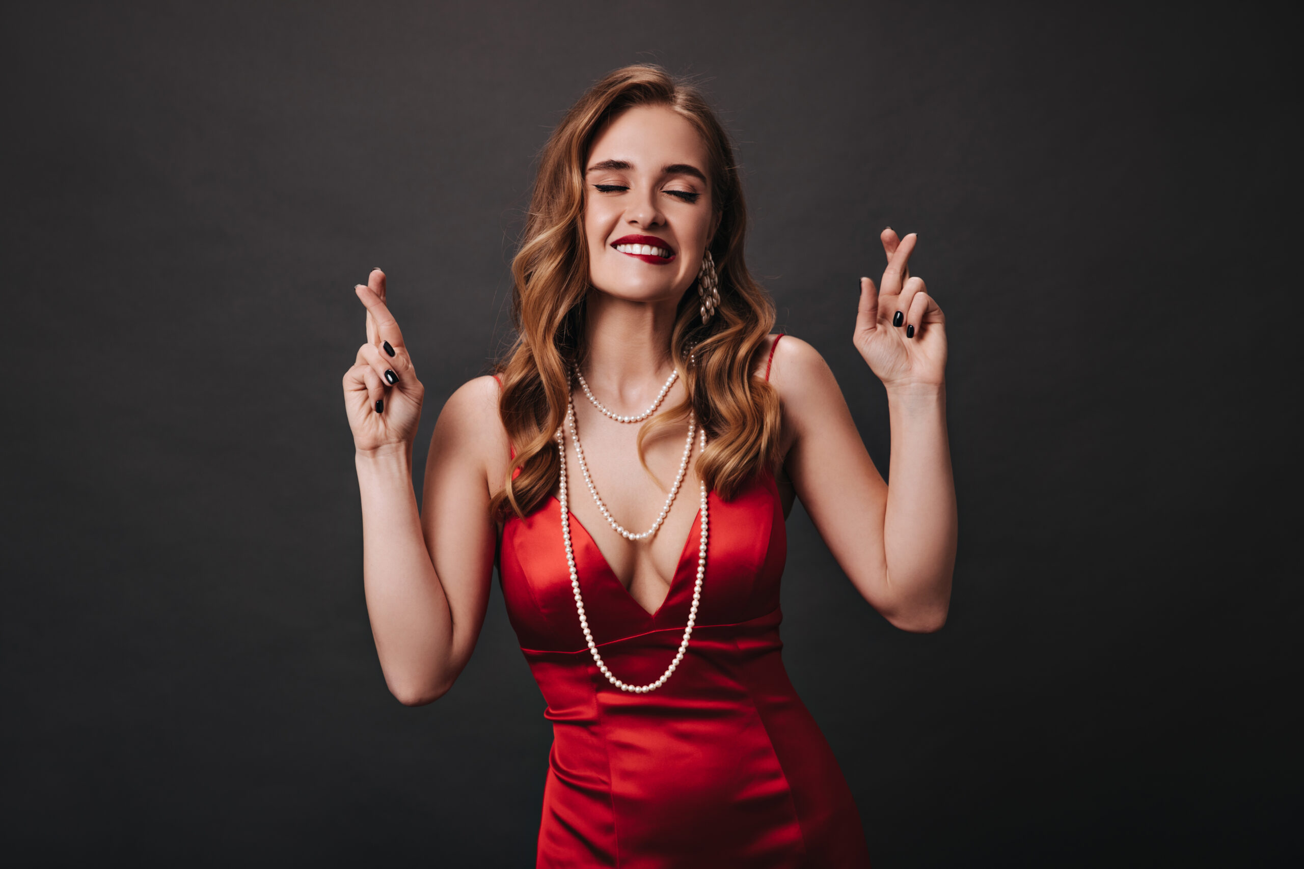Cool lady in red silk outfit crosses fingers on black background. Blonde curly woman in satin dress Cool lady in red silk outfit crosses fingers on black background. Blonde curly woman in satin dress